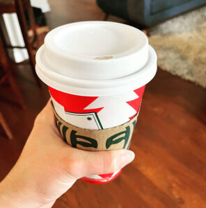 A hand holding a red Starbucks coffee cup